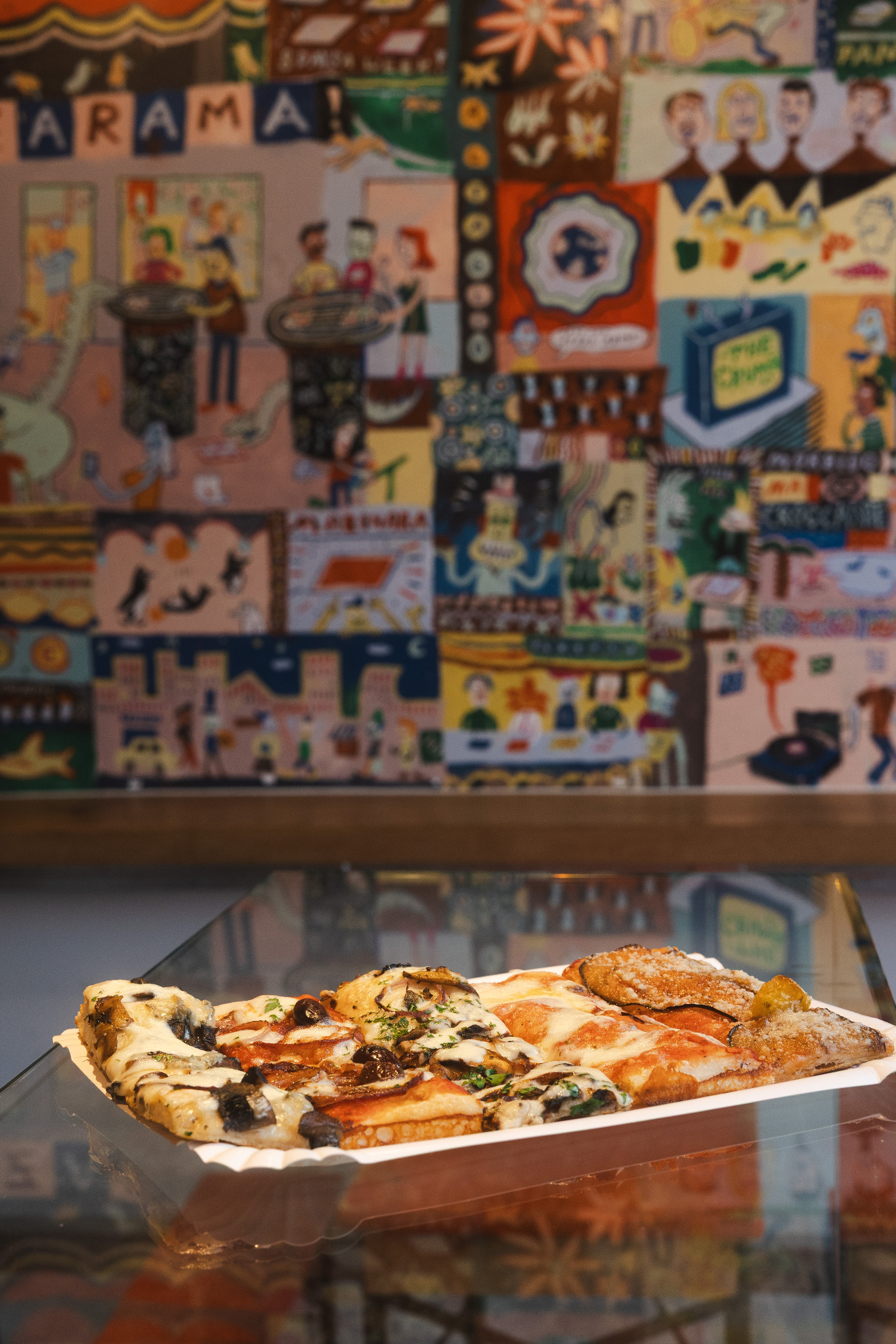 Assorted pizza slices in front of Pizzarama's painted art wall